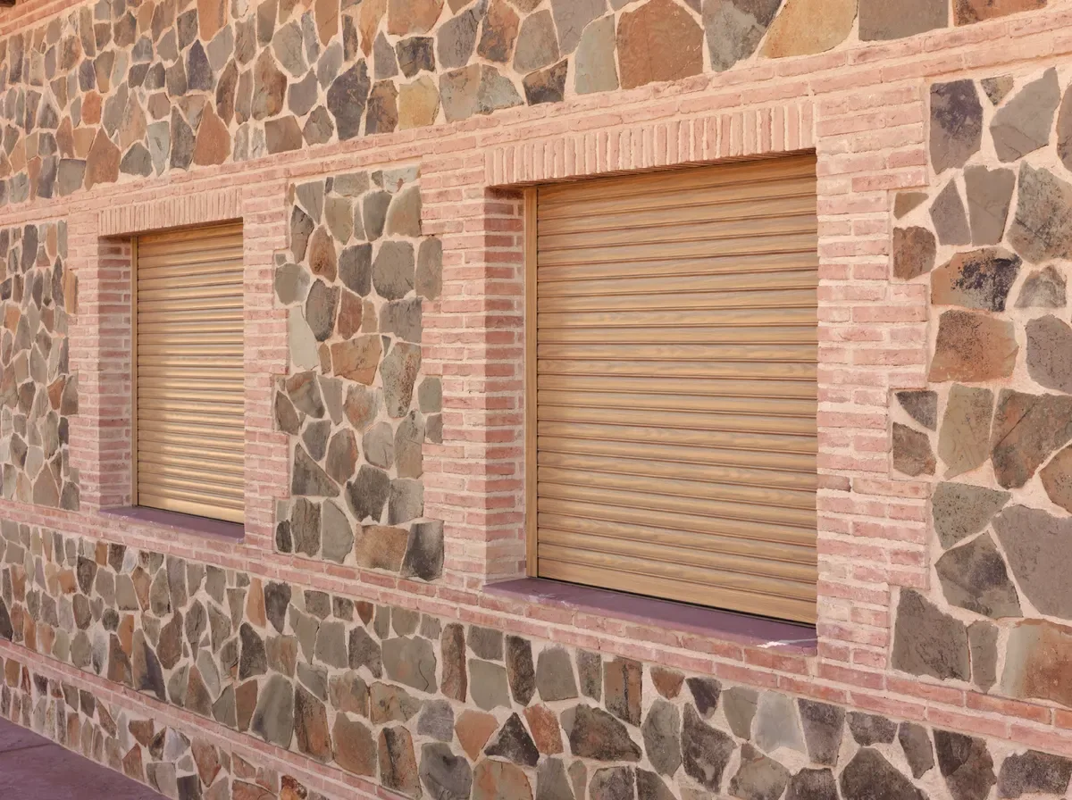 Dos persianas enrollables nuevas en tono madera en una fachada de piedra y ladrillo